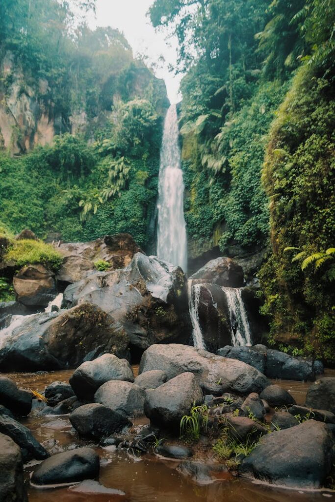 Beautiful Indonesian waterfall cascading through lush green forest, surrounded by rocks and flowing streams.