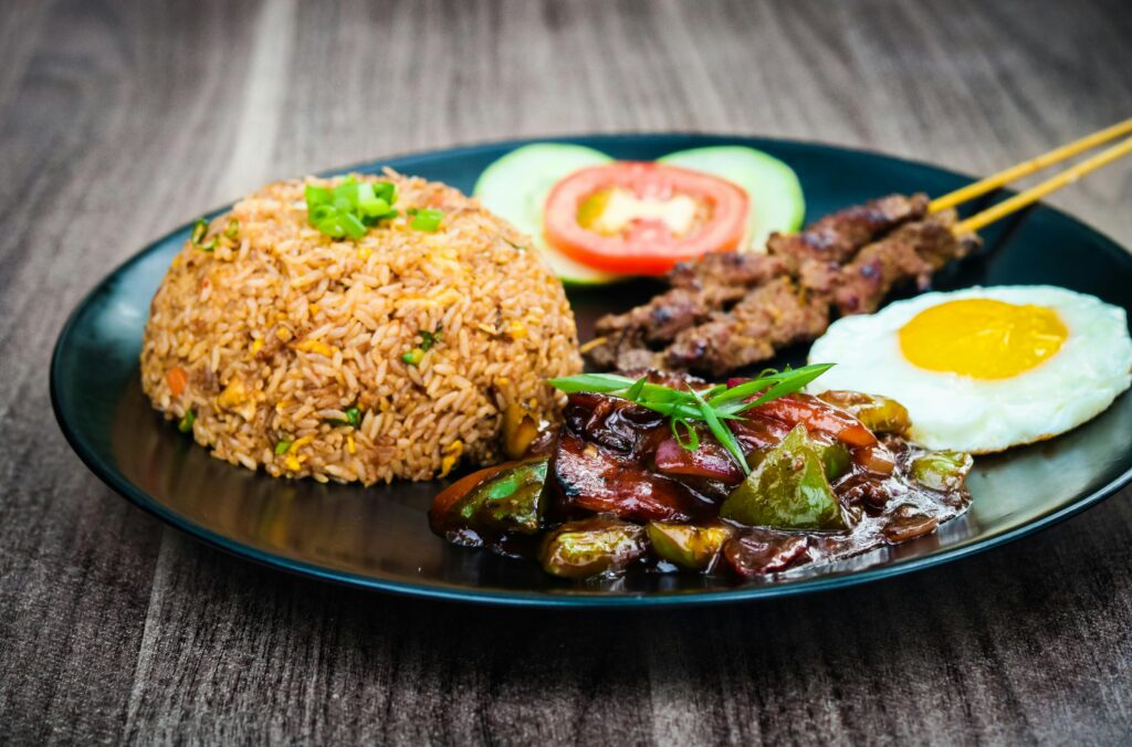 Appetizing Nasi Goreng served with satay, fried egg, and vegetables on a black plate.